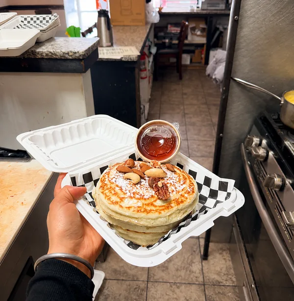 Pancakes topped with nuts and powdered sugar, with syrup at Nena’s
